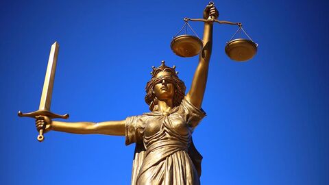 Goldfarbene Justitia-Statue vor blauem Hintergrund