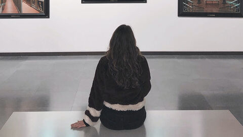 Frau sitzt auf einer Bank in einer Galerie und betrachtet Bilder.